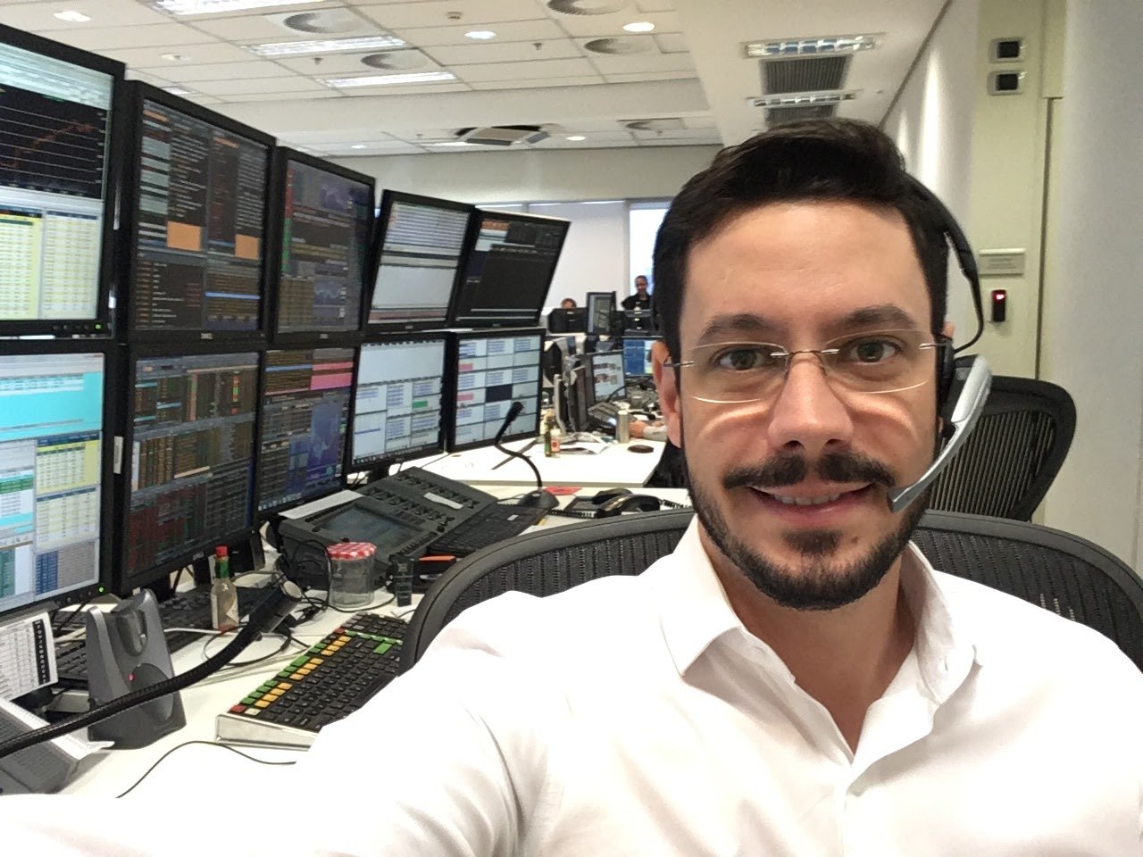 Gustavo Carvalho dos Santos na mesa de operações, com múltiplos monitores de mercado ao fundo